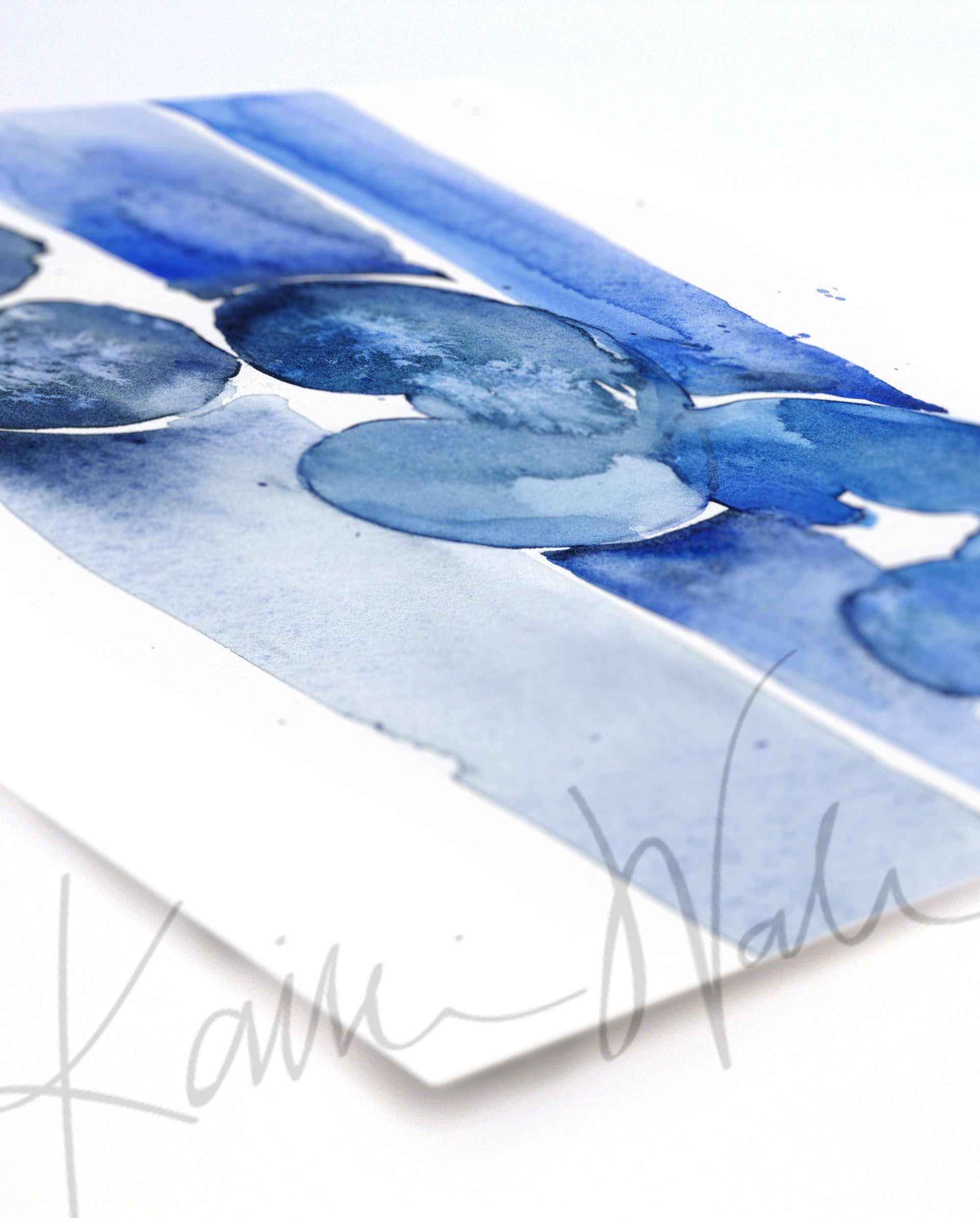 A watercolor painting of three kidneys in blues and navy printed on paper at an angle. You can see the thickness of the paper. The anatomy watercolor print is crisper at the front and blurry as the paper gets further away.