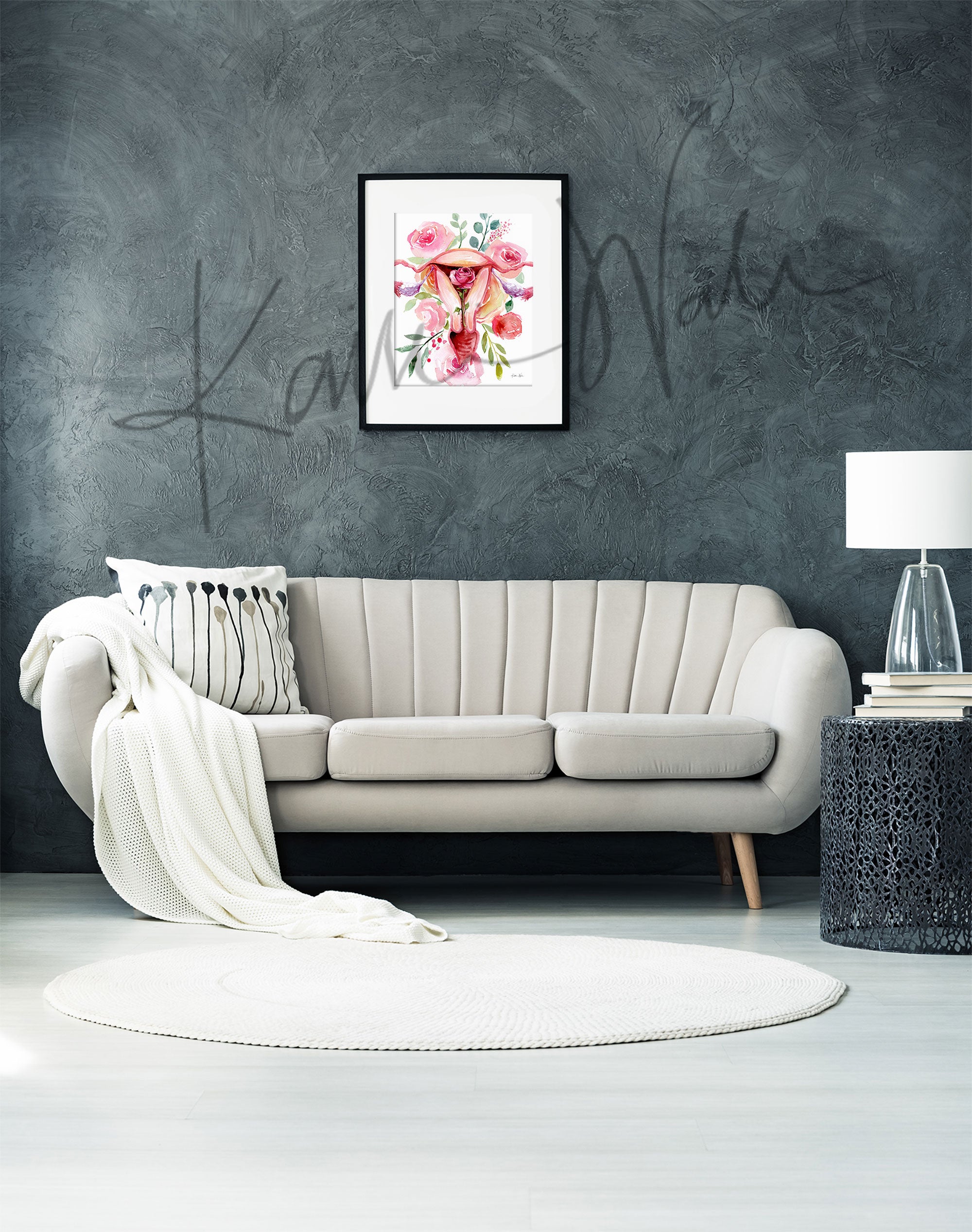 Framed watercolor painting of a uterus with flowers around. The painting is hanging over a white couch.