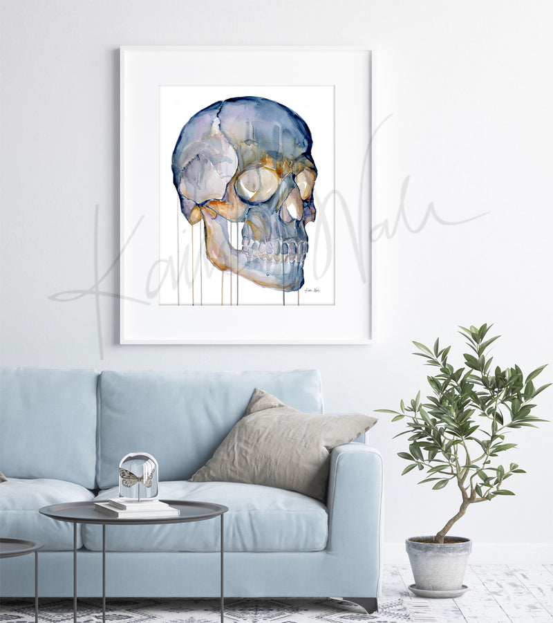 Framed watercolor painting of a skull from a three quarter view. The painting is hanging over a blue couch.